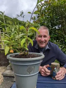 Scott smiling at the camera, a plant is in front of him