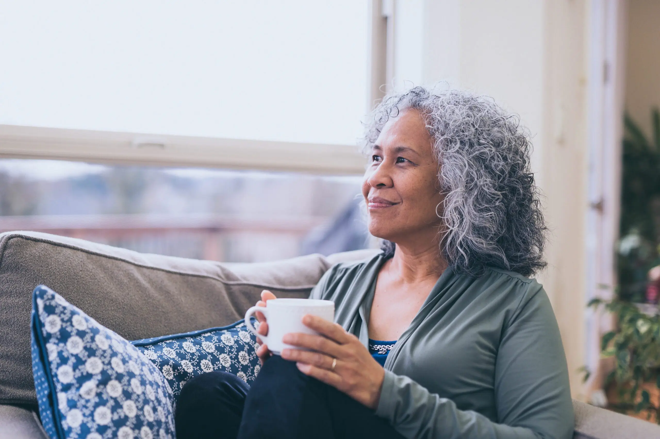 Lady holding a mug looking out of the window smiling