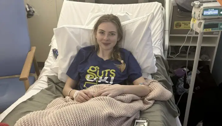 Elle is smiling and sat up on a hospital bed wearing a Guts UK t-shirt.