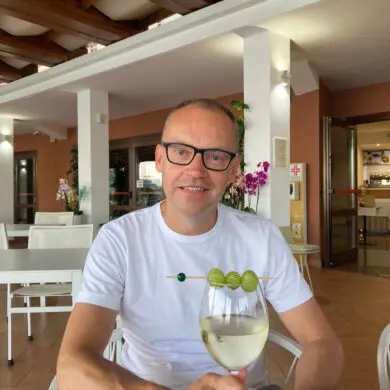 Jonald is sitting in a restaurant on holiday, smiling, with a glass of white wine in front of him