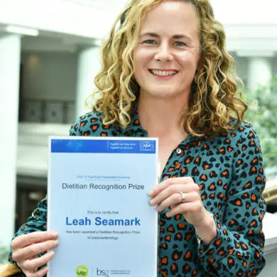 Leah is holding her certificate and smiling at the camera.