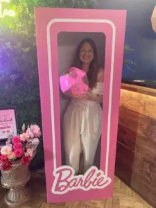 Sian is smiling and holding a pink and transparent inflatable beach ball. She is standing inside a pink human sized box which says Barbie on the bottom.