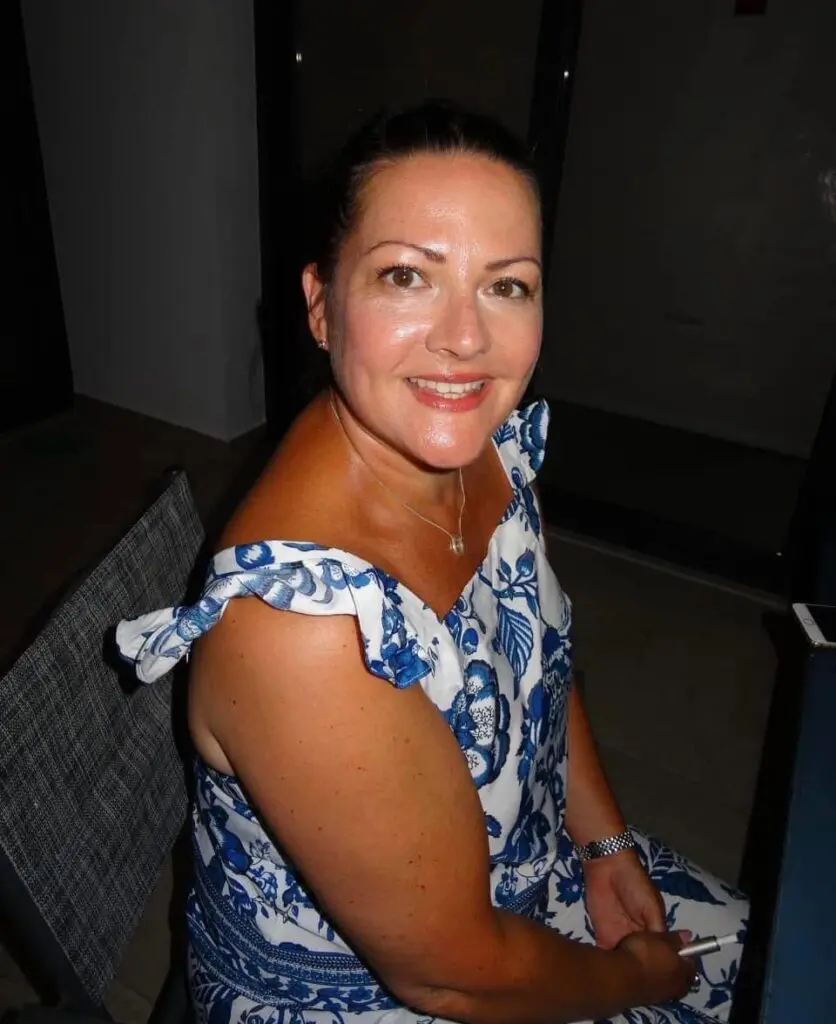 Paula is on holiday in Cyprus, ready for a night out. The photo is taken from slightly above her, and she smiles at the camera. She is wearing a white and blue floral dress, with frilly straps over her shoulders.