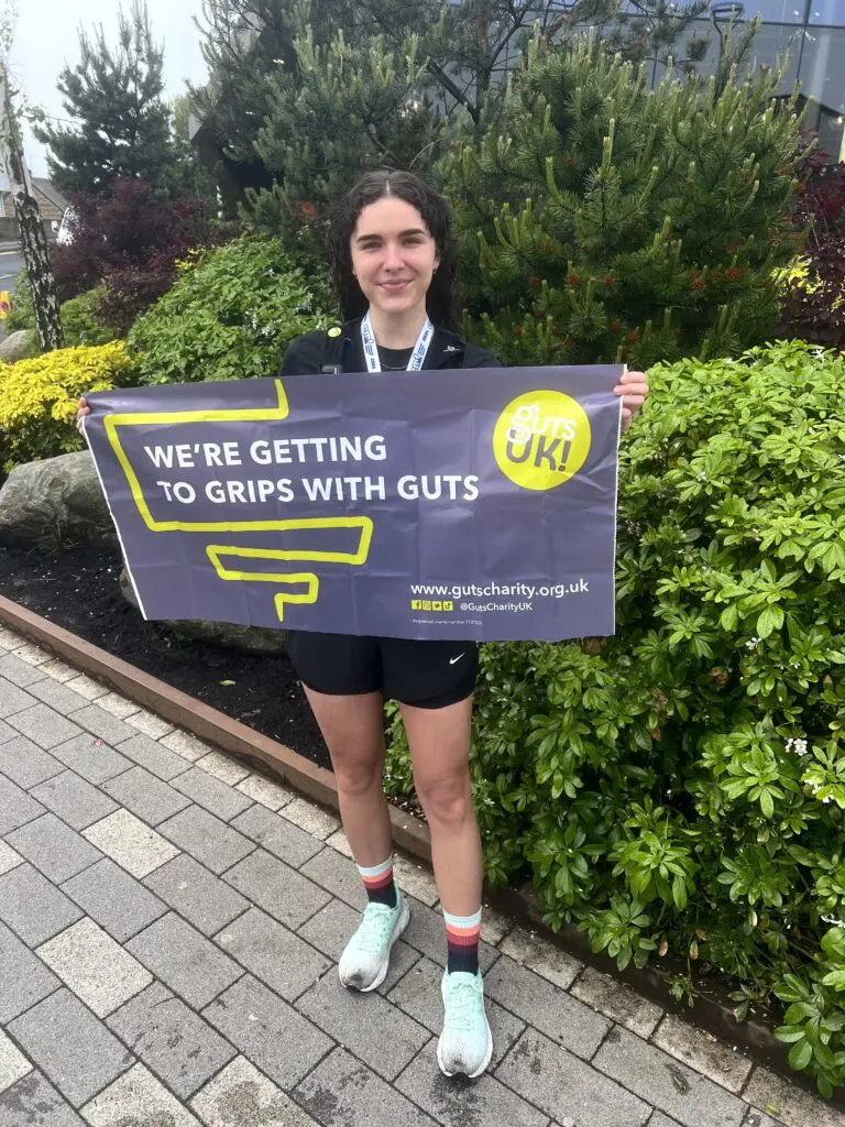 Briony is holding a Guts UK banner and is standing after running the Edinburgh Half Marathon.