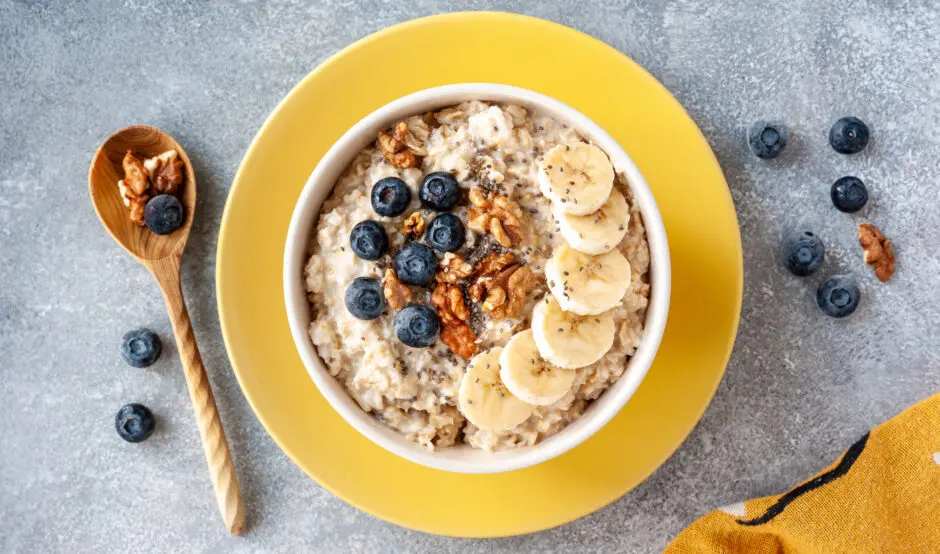 A yellow bowl with porridge, blueberries, banana and nuts.