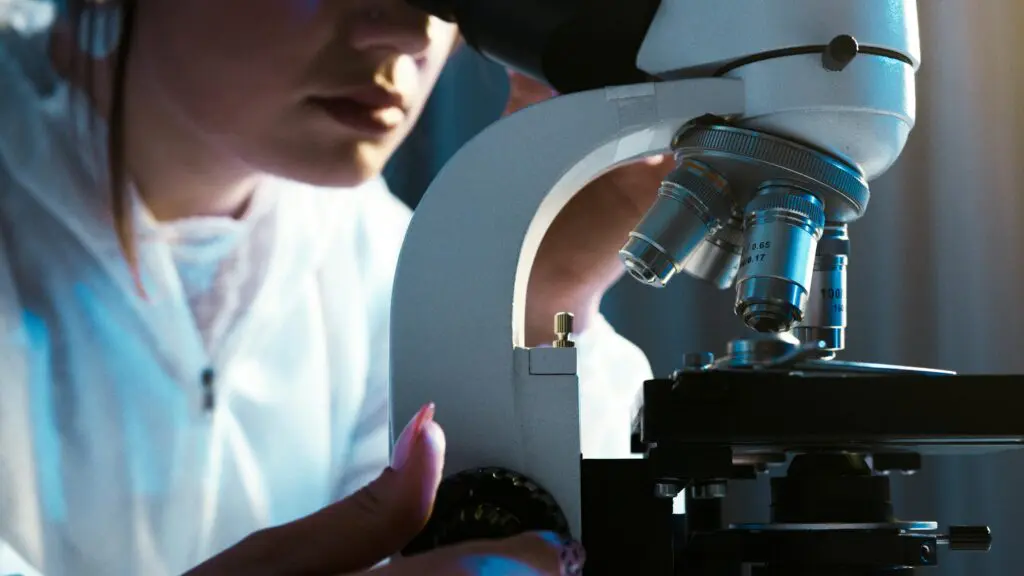A female in a white lab coat is looking into a microscope