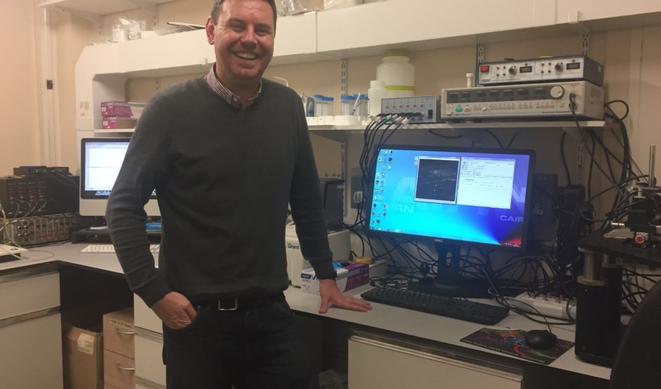 Dr Conor McCann standing by his computer in his laboratory