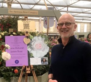 Garry smiling next to a rose that has been named after Dame Deborah James aka bowelbabe