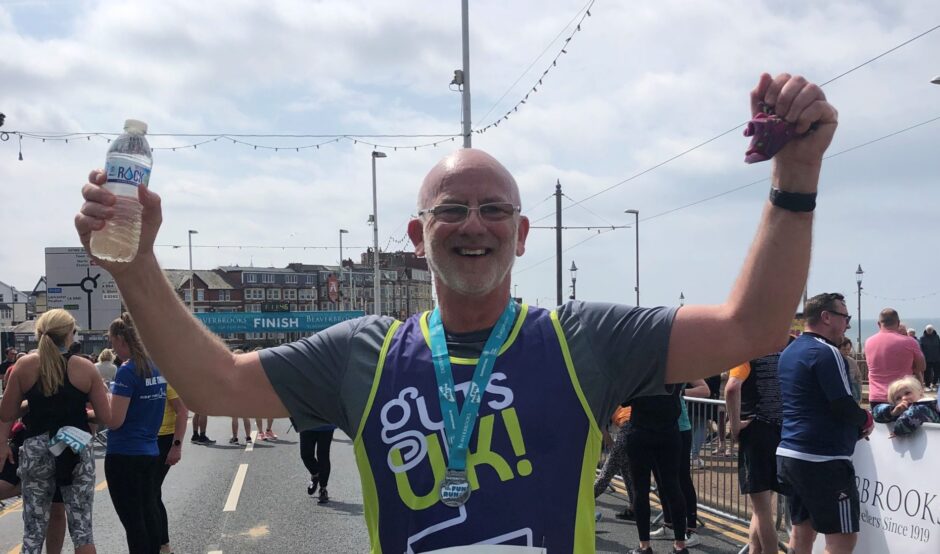 Garry looking happy with his hands in the air after completing a 10k run in his Guts UK running vest