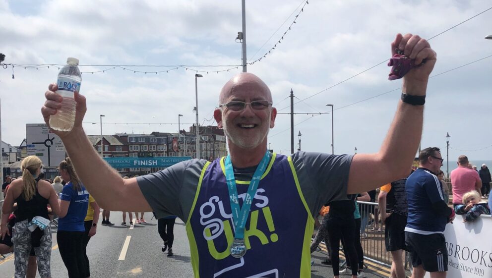 Garry looking happy with his hands in the air after completing a 10k run in his Guts UK running vest