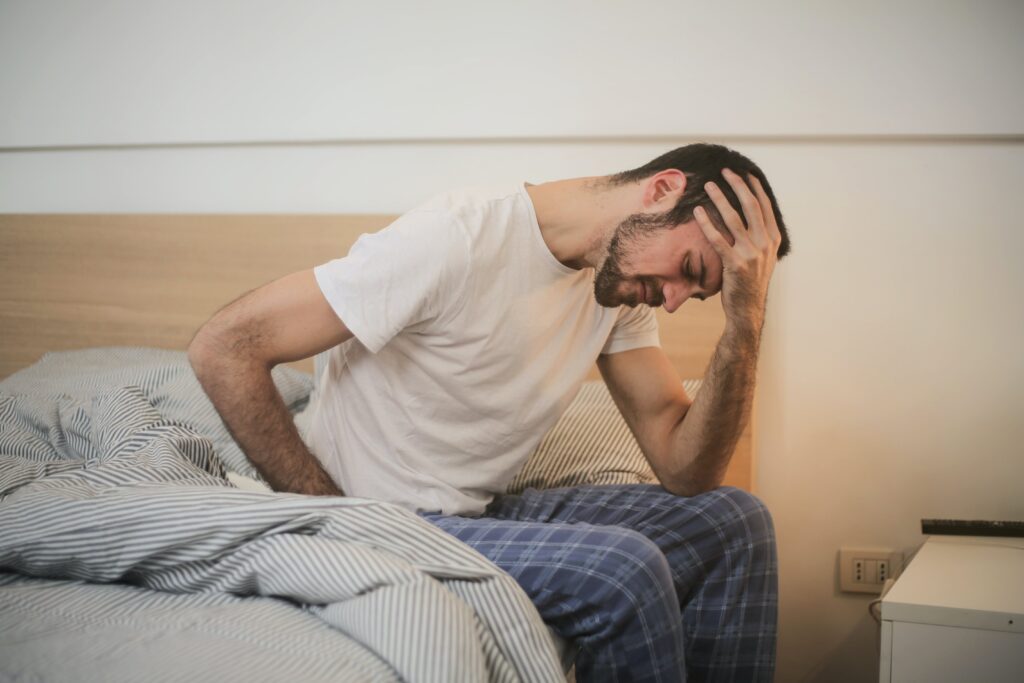 Man sitting on the edge of the bed in pain, clutching his stomach and head