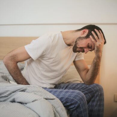 Man sitting on the edge of the bed in pain, clutching his stomach and head