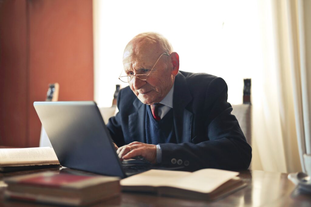 Elderly man sat at a desk, browsing his laptop