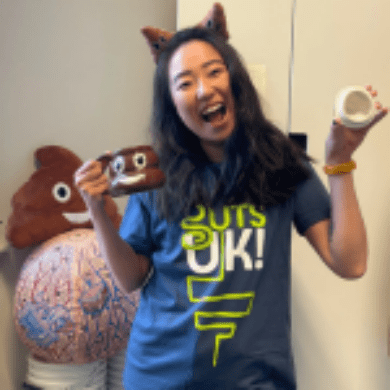 Leeona is smiling towards the camera. She is wearing a navy t-shirt, with the Guts UK logo on and is holding a poop emoji mug to the right of her, with the lid in her left hand.
