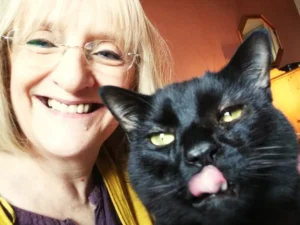 Julie is taking a selfie with her black cat named Stoker. Julie is smiling at the camera and Stoker is licking his lips.