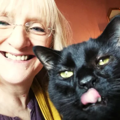 Julie is taking a selfie with her black cat named Stoker. Julie is smiling at the camera and Stoker is licking his lips.