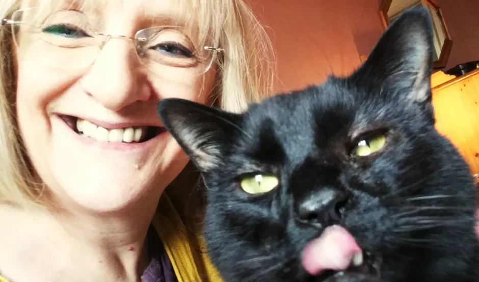 Julie is taking a selfie with her black cat named Stoker. Julie is smiling at the camera and Stoker is licking his lips.