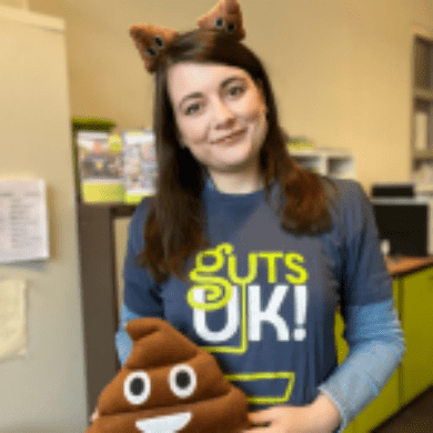 Amy is wearing a Guts UK t-shirt and is holding a poop emoji cushion and poop emoji boppers headband