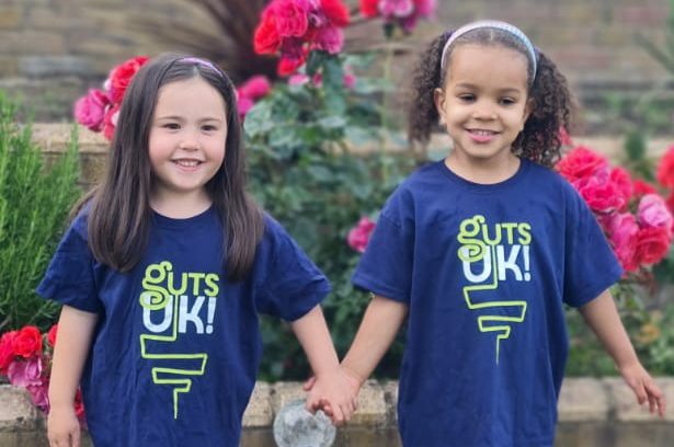 Grace and Alia are smiling at the camera in their Guts UK t shirts and holding hands.
