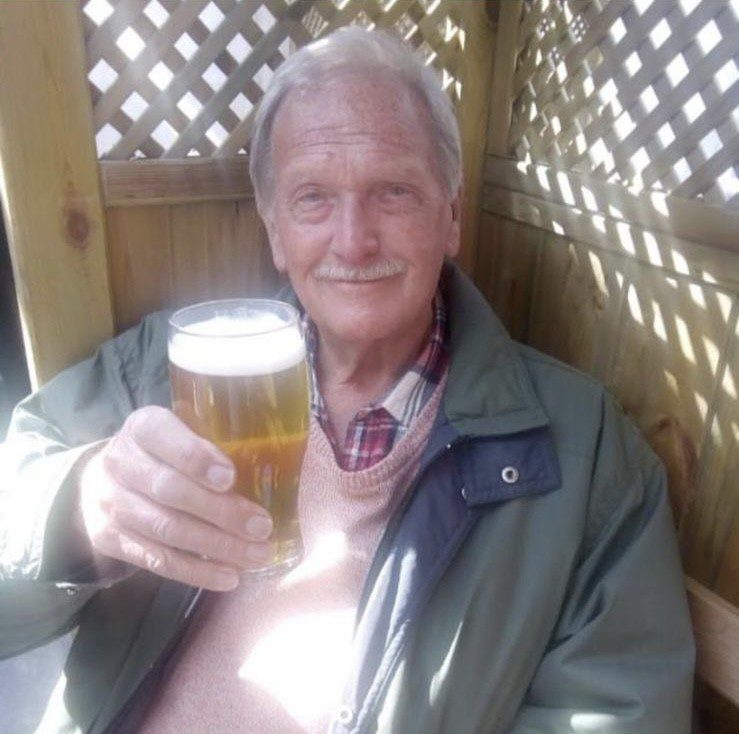 Tony is smiling at the camera, sat in a pub garden with a pint of beer.