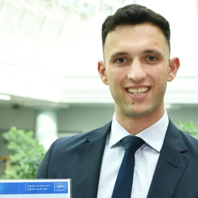 Leon holds his certificate and is smiling at the camera.