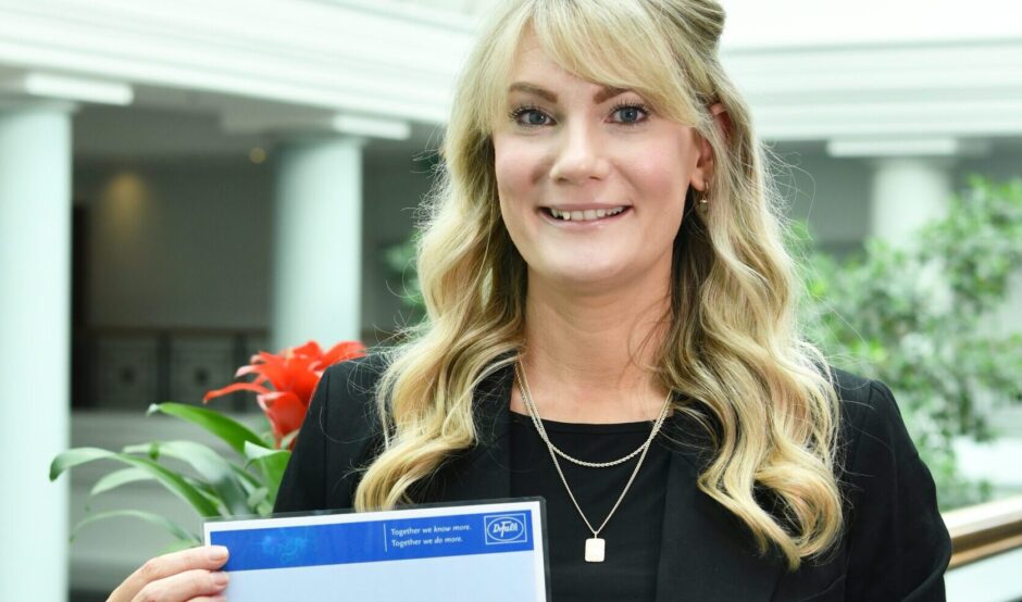 Laura is holding her awards certificate and smiles at the camera