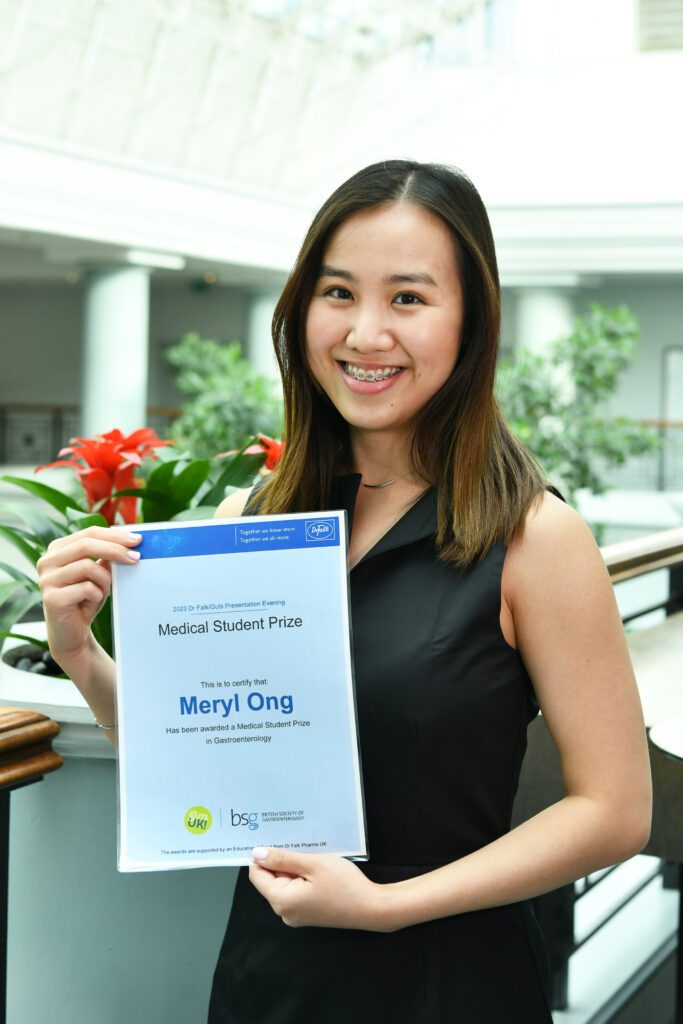 Meryl is holding her awards certificate and is smiling at the camera