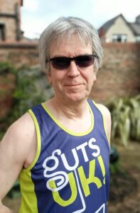 Steve is smiling at the camera. He is wearing sunglasses and a Guts UK running vest.