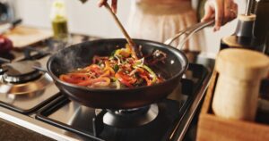 A person cooking vegetables in a pan.