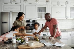 Two adults and two children are happily gathered around a table filled with food in the kitchen. 