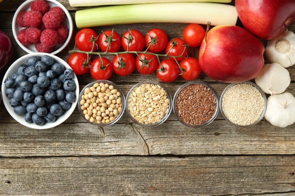 Different fresh products a wooden table including raspberries, blueberries, tomatoes, leeks, pulses and seeds, apples and garlic.