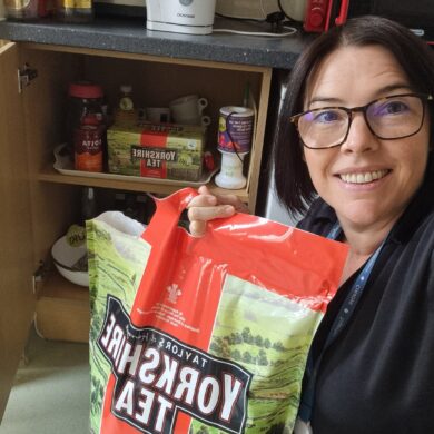 Catherine, holding a big bag of Yorkshire Tea Bags next to an open kitchen cupboard.