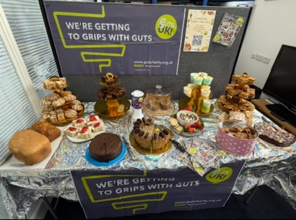 A table full of cakes, with a banner behind the table and pinned to the table promoting Guts UK