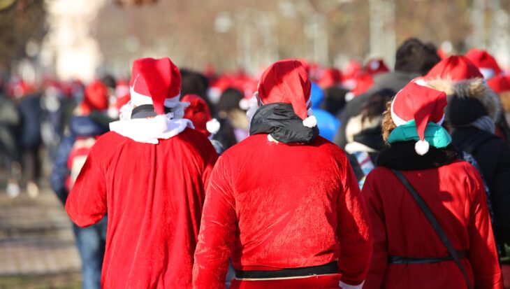 A crowd of people walk together wearing red Santa hats and costumes.