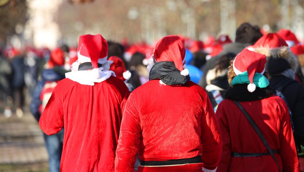 A crowd of people walk together wearing red Santa hats and costumes.