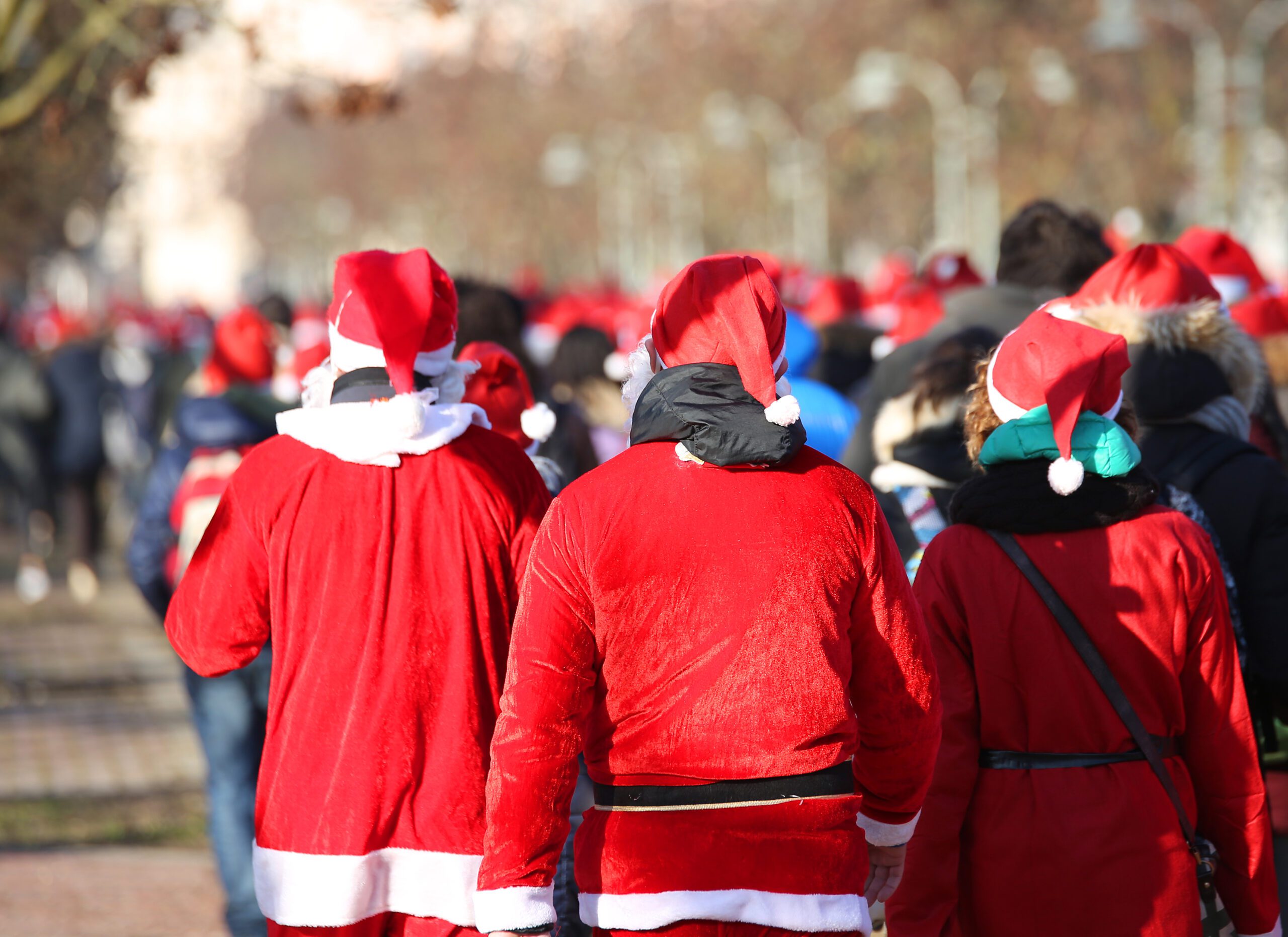 A crowd of people walk together wearing red Santa hats and costumes.