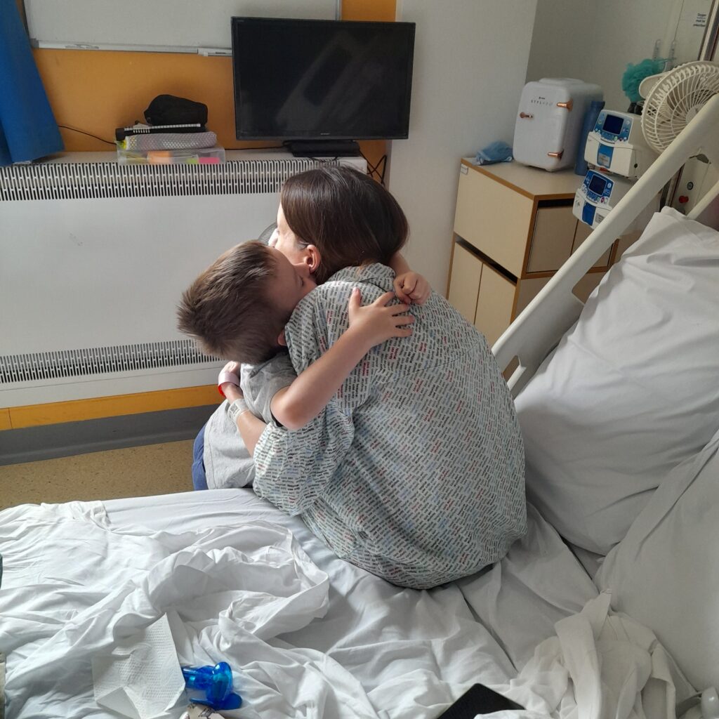 Lisa is having cuddles with George, sat on the edge of her hospital bed.