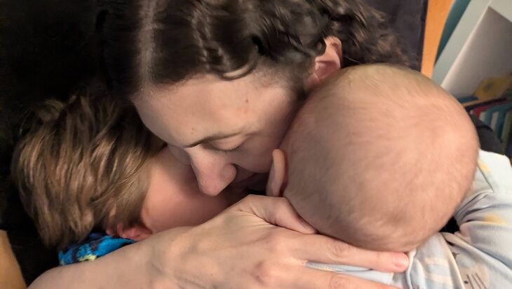 Rachael embraces her two children closely. They are sat on a wooden chair.