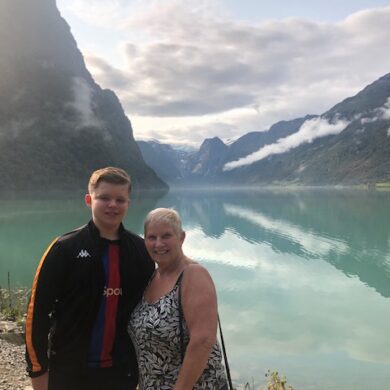 Sue (left) stands with her grandson with a backdrop of the Norwegian fjords.