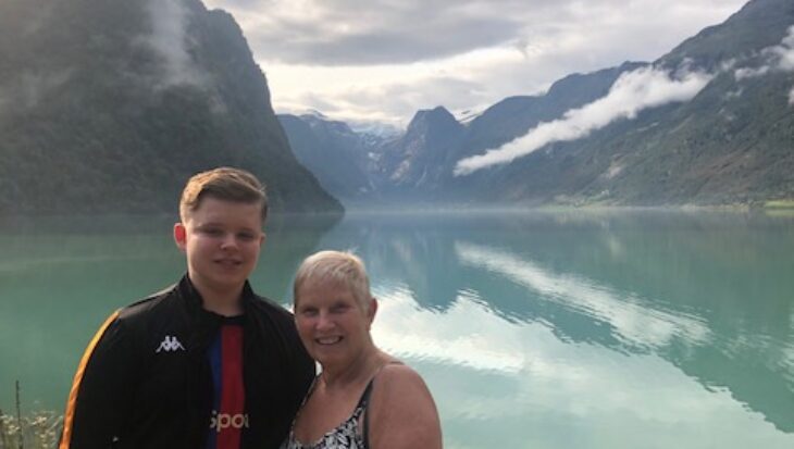 Sue (left) stands with her grandson with a backdrop of the Norwegian fjords.