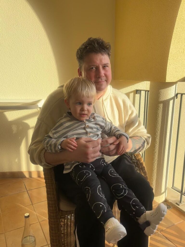 Mark is sitting down with his nephew on his knee.