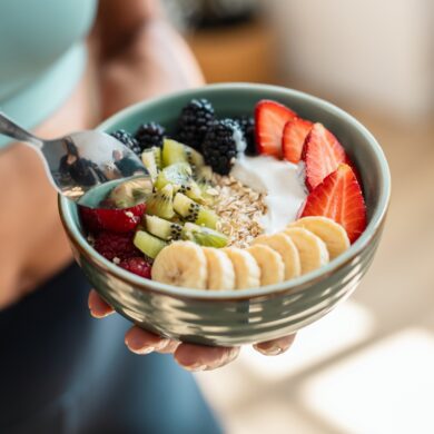 A person eating a yogurt bowel with fruit and nuts.