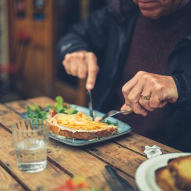 A man sits at a table eating a meal with a knife and fork.