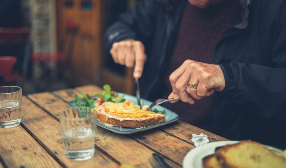 A man sits at a table eating a meal with a knife and fork.